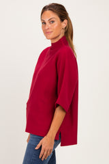 woman wearing a red short sleeve mock neck top with side slits and a relaxed fit, paired with blue jeans
