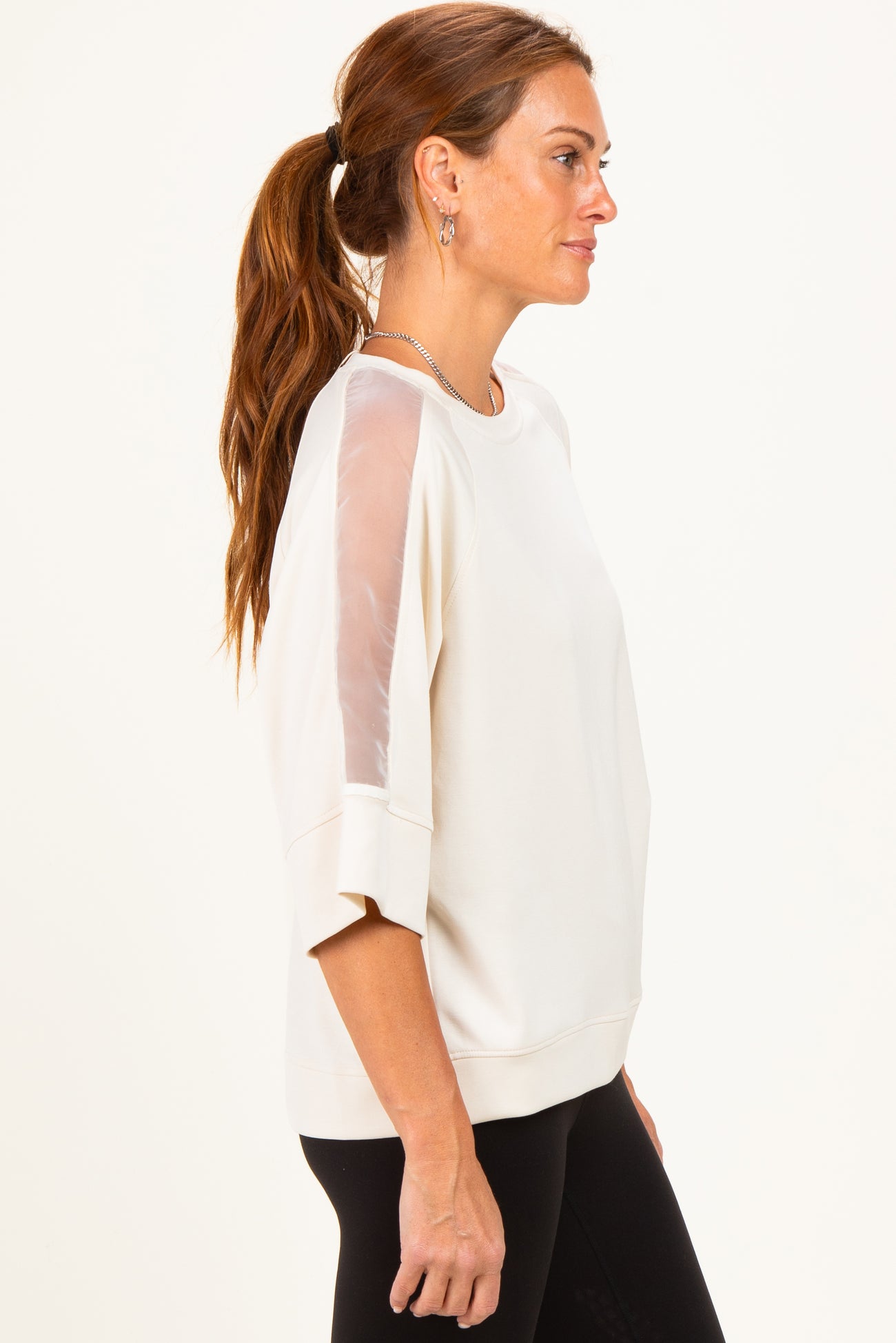 woman wearing a cream-colored sweatshirt with sheer sleeves and a relaxed fit