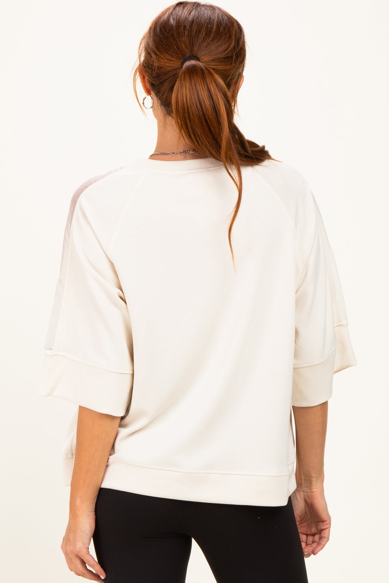 woman wearing a beige oversized sweatshirt with short sleeves and a relaxed fit, viewed from the back