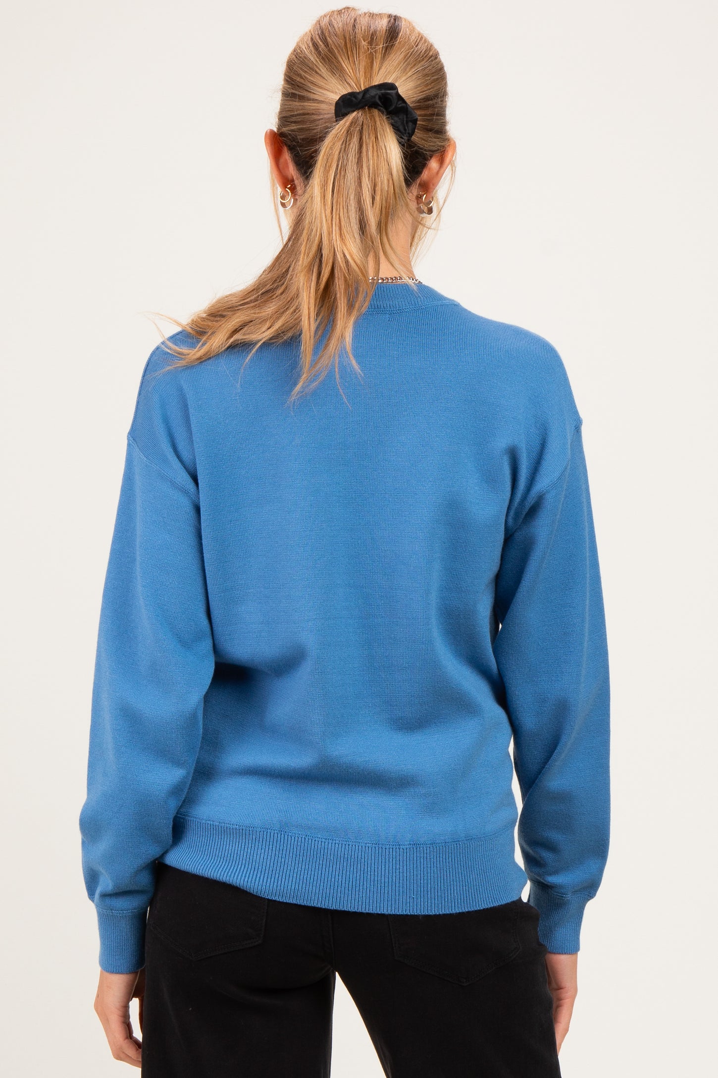 woman wearing a blue maternity sweater, shown from the back, paired with black pants