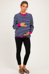 woman wearing a navy and white striped maternity sweatshirt with pink accents and holding her baby bump, paired with black leggings