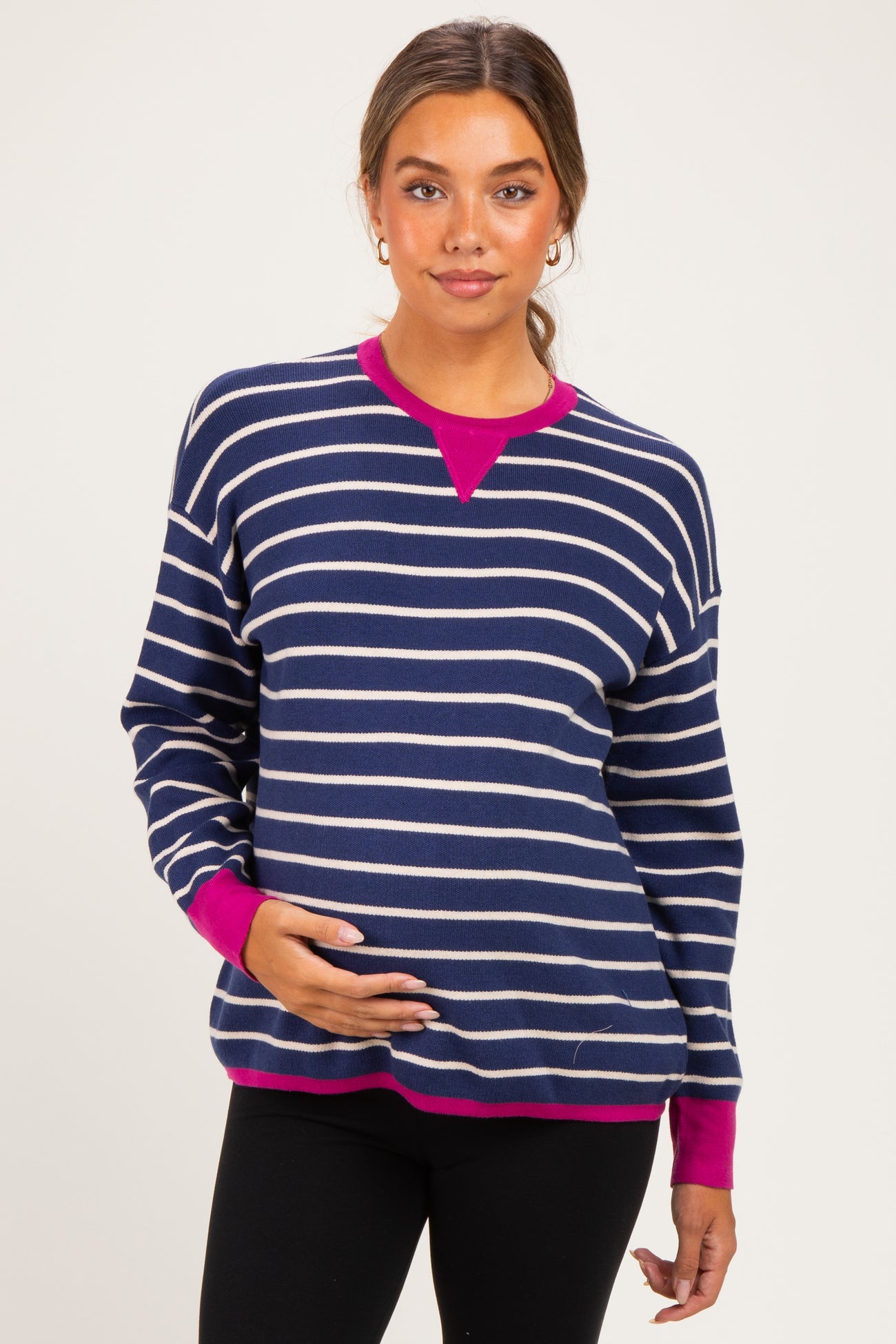 woman wearing a navy and white striped maternity sweater with pink accents and holding her baby bump