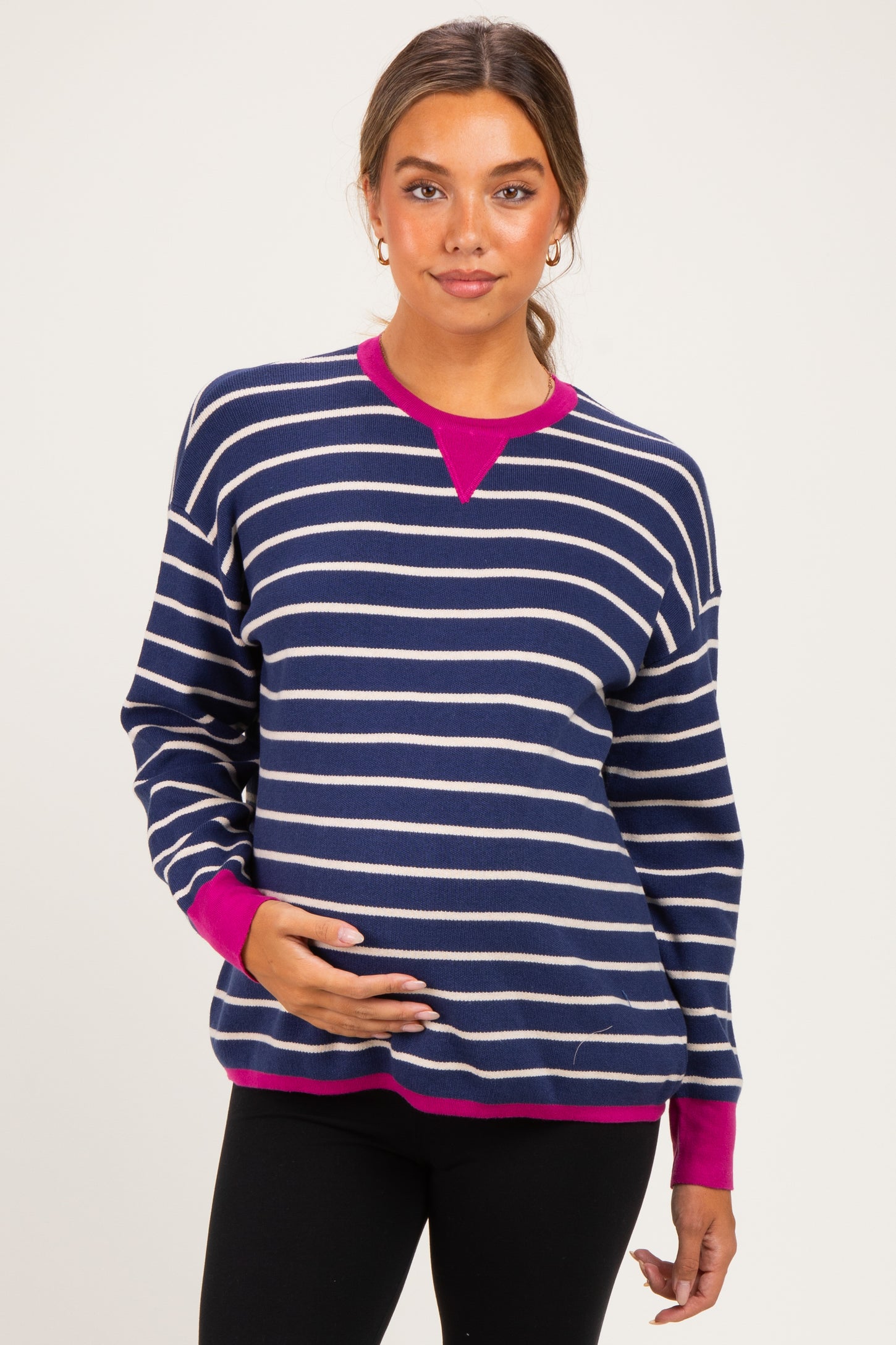 woman wearing a navy and white striped maternity sweater with pink accents and holding her baby bump