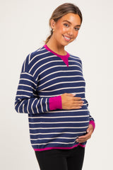 woman wearing a navy blue and white striped maternity sweater with pink accents, holding her baby bump