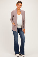 woman wearing a light mauve maternity cardigan over a white top and blue flared jeans, showing her baby bump