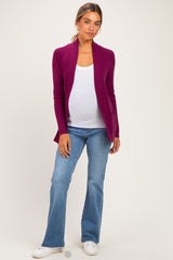woman wearing a deep purple maternity cardigan over a white tank top and blue flared jeans, showing her baby bump