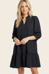 woman wearing a black tiered mini dress with a collar and three-quarter puff sleeves