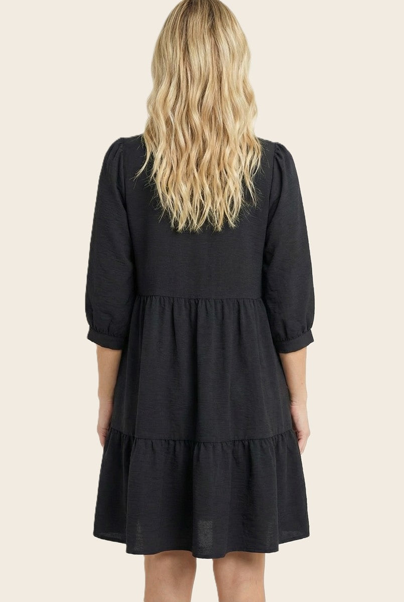 woman wearing a black tiered dress with three-quarter puff sleeves, shown from the back