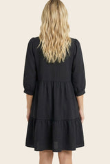 woman wearing a black tiered dress with three-quarter puff sleeves, shown from the back