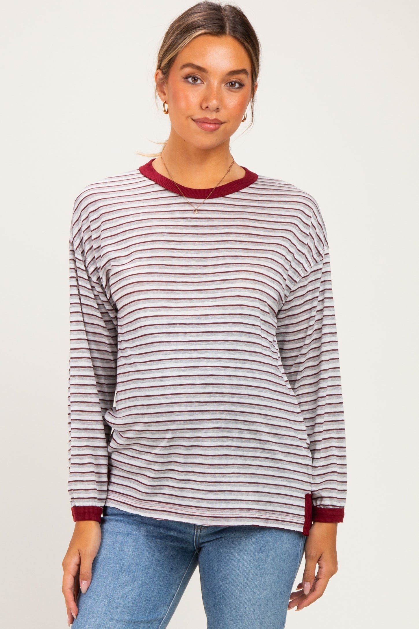 woman wearing a striped long sleeve maternity top with burgundy accents and light blue jeans