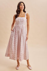 woman wearing a light pink floral maxi dress with a fitted bodice and pockets, styled with ballet flats