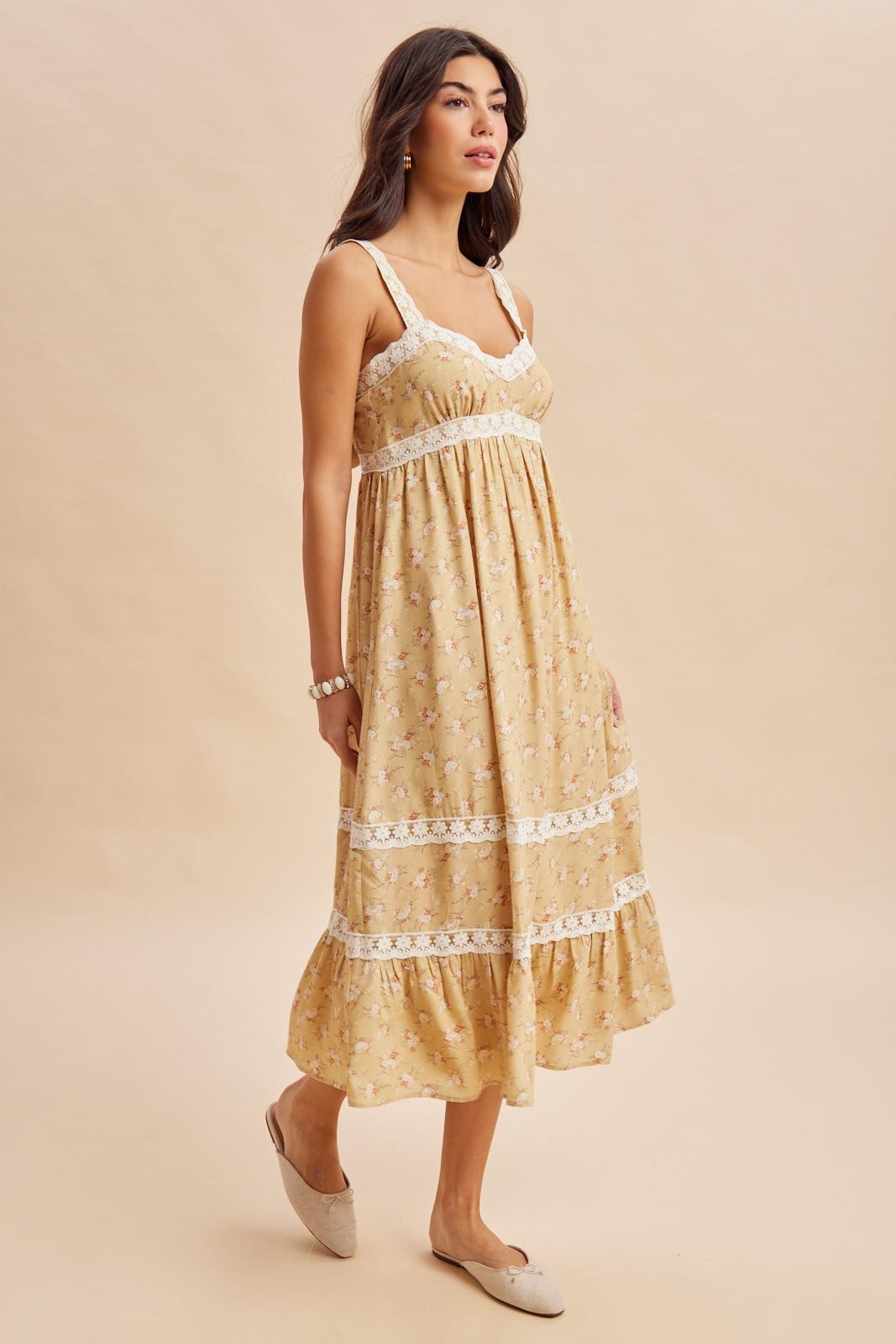 woman wearing a yellow floral maxi dress with lace details and a flowy skirt, standing against a neutral background
