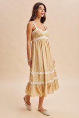 woman wearing a yellow floral maxi dress with lace details and a flowy skirt, standing against a neutral background