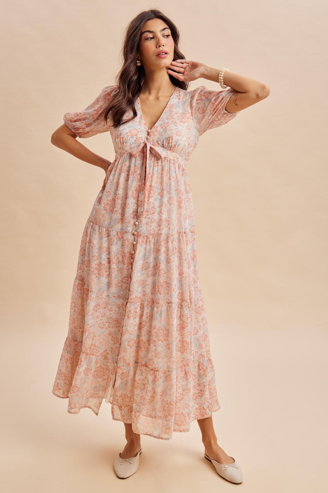 woman wearing a pink floral maxi dress with short puff sleeves and a tie-front detail