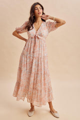 woman wearing a pink floral maxi dress with short puff sleeves and a tie-front detail