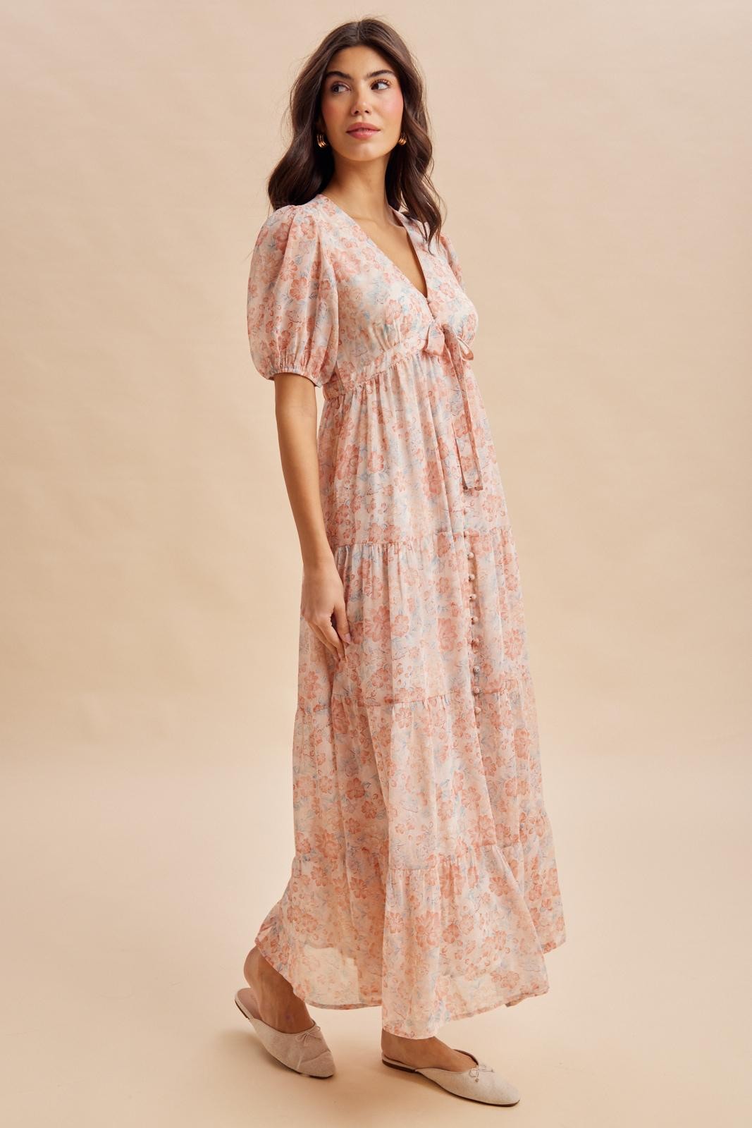 woman wearing a light pink floral maxi dress with puff sleeves and a tie front detail