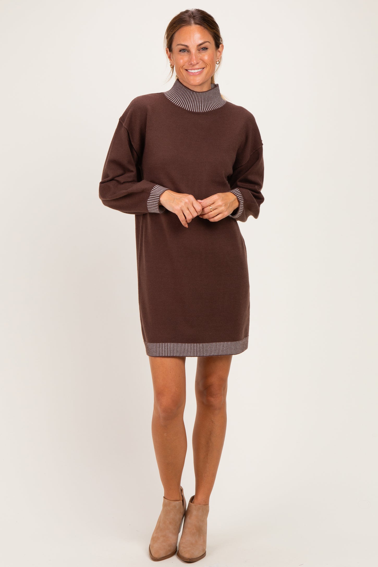 woman wearing a brown sweater dress with a ribbed collar and cuff details, standing and smiling