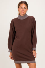 woman wearing a brown sweater dress with a striped collar and sleeves, standing with a smile