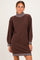 woman wearing a brown sweater dress with a striped collar and sleeves, standing with a smile