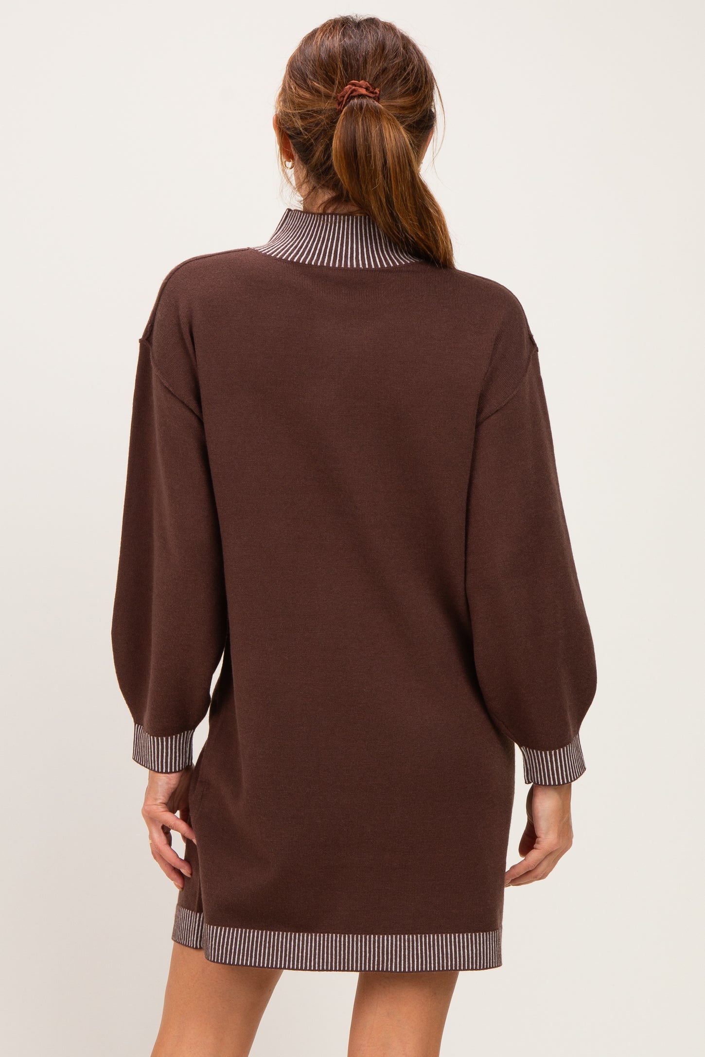 woman wearing a brown sweater dress with long sleeves and striped cuffs, showing the back view