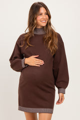 woman wearing a brown maternity sweater dress with striped details and holding her baby bump