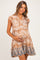 woman wearing a tan floral print maternity dress with ruffle sleeves and holding her baby bump