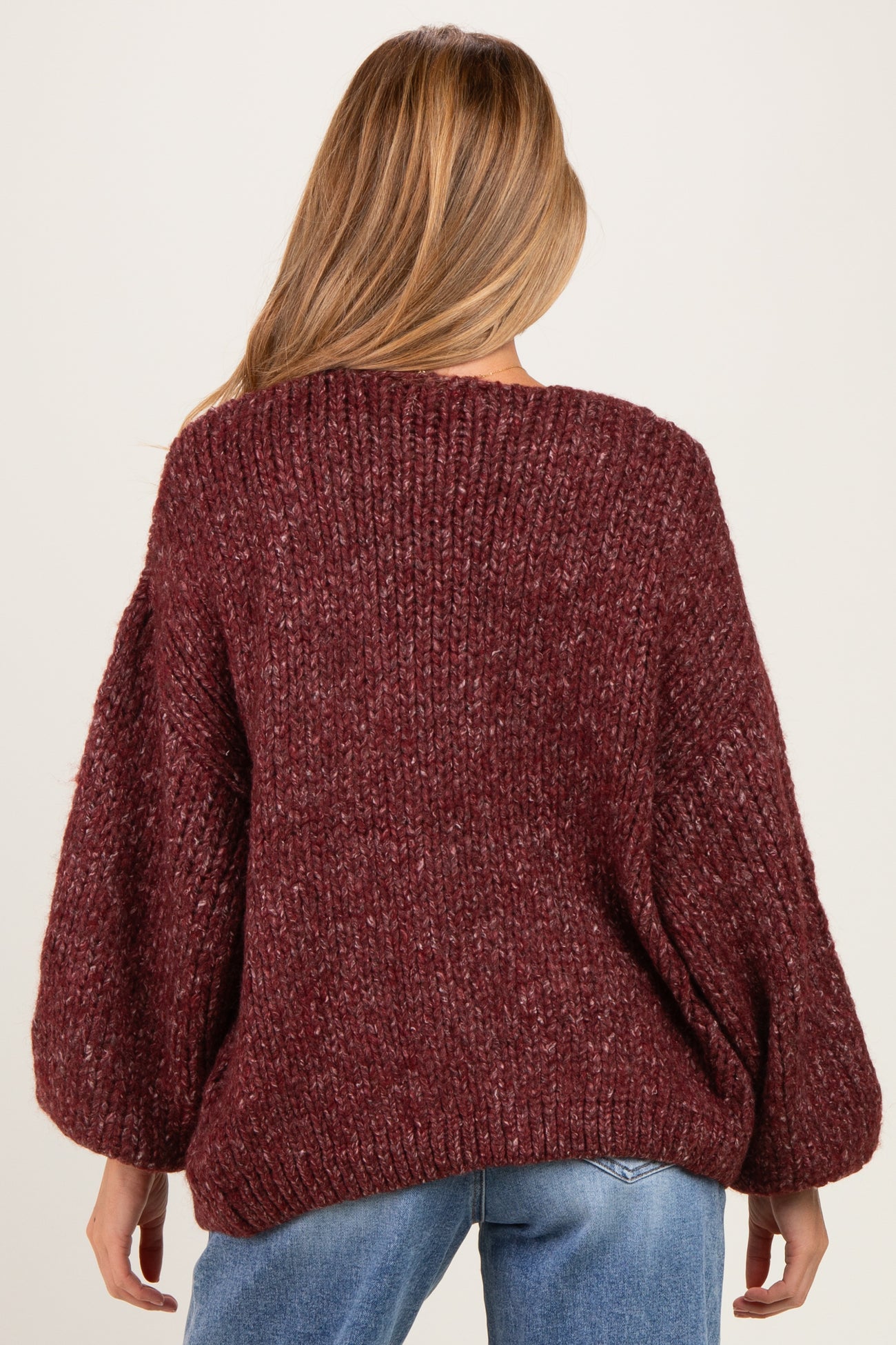 woman wearing a burgundy chunky knit maternity sweater with balloon sleeves, seen from the back
