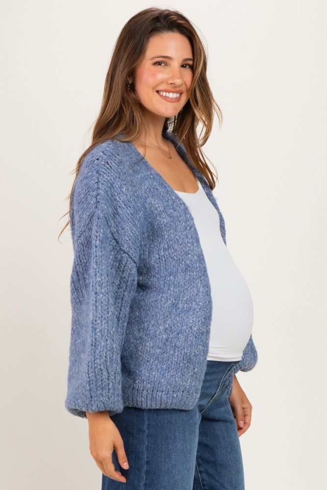 woman wearing a light blue maternity cardigan over a white top and showing her baby bump, smiling