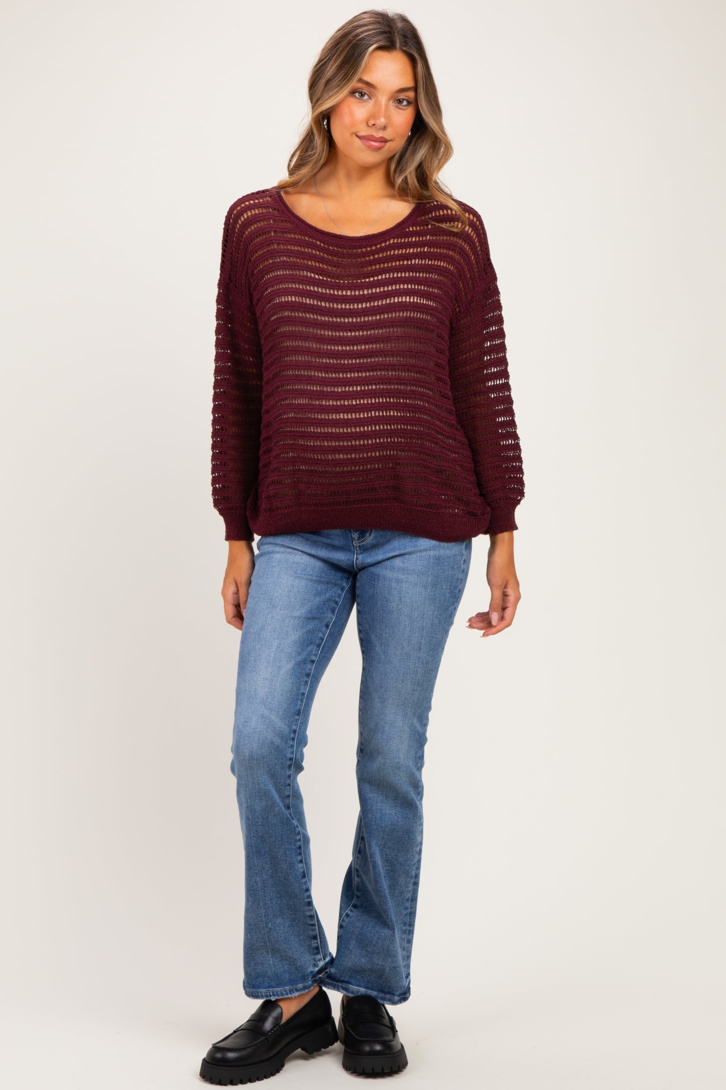 woman wearing a burgundy open knit maternity sweater with long sleeves and blue flared jeans