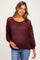 woman wearing a maroon open-knit maternity sweater, holding her baby bump, paired with blue jeans