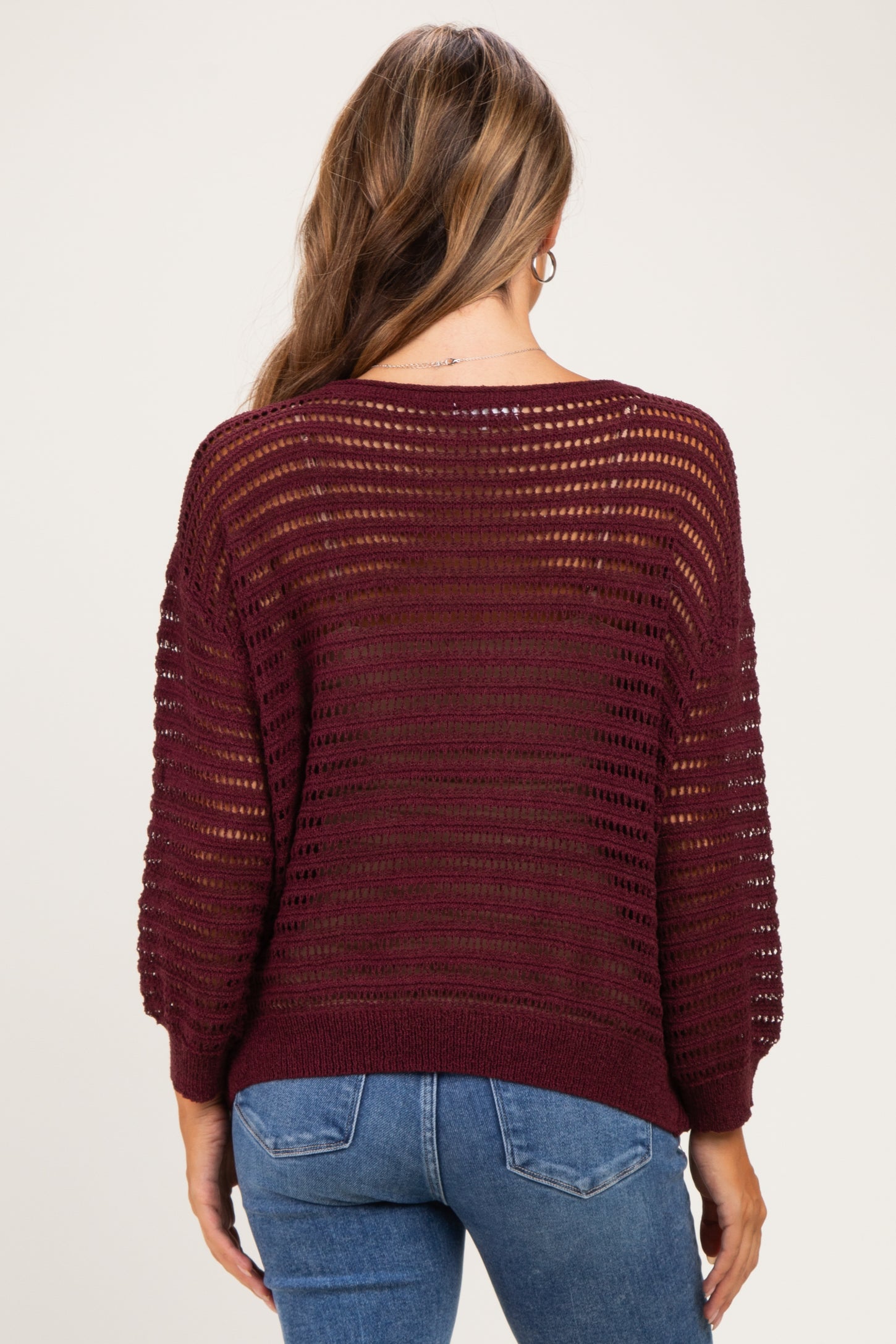 woman wearing a burgundy open knit maternity sweater with a relaxed fit and three-quarter sleeves, seen from the back