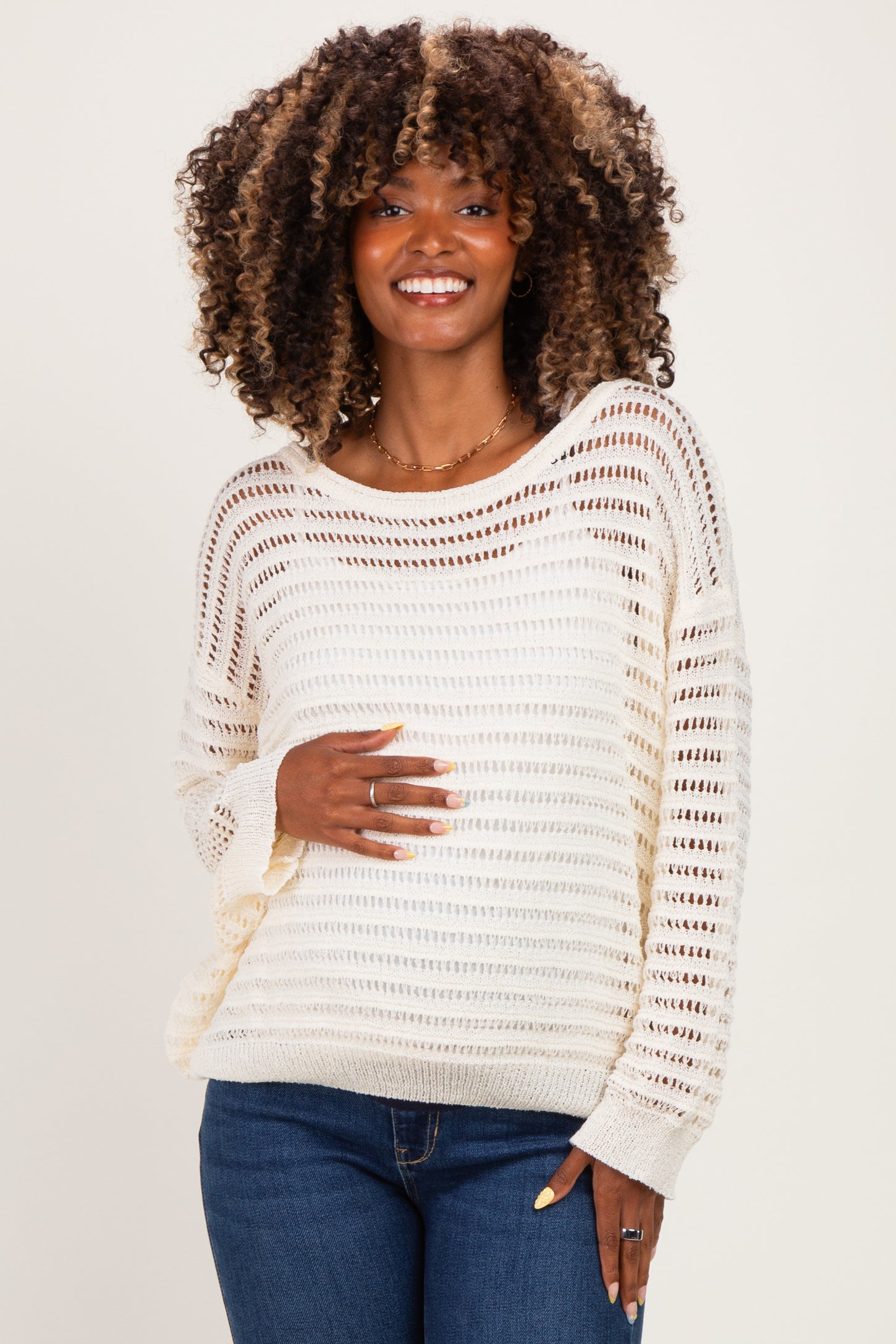 woman wearing a cream lightweight crochet maternity sweater and showing her baby bump