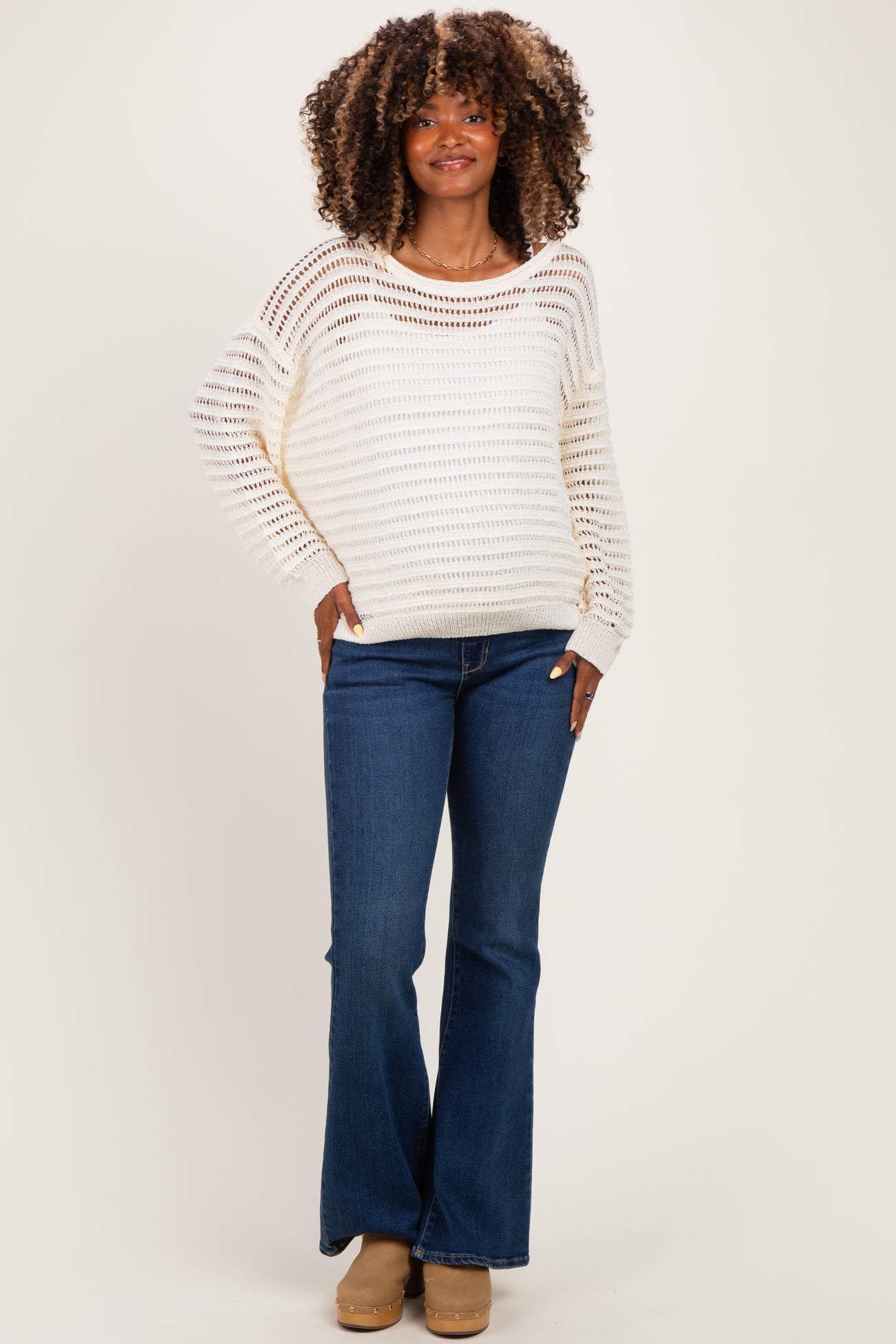 woman wearing a cream striped maternity sweater with a relaxed fit and blue flared maternity jeans