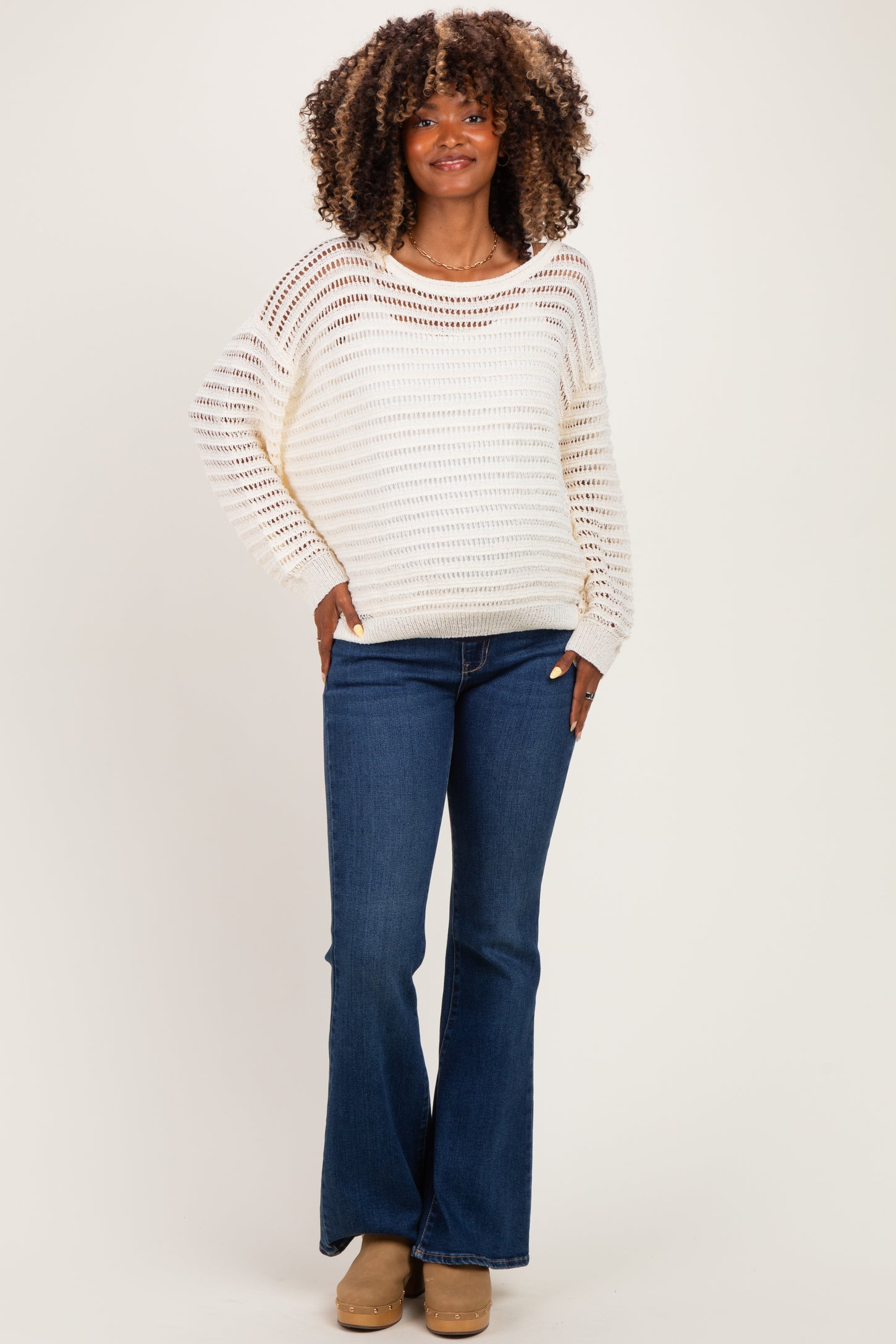 woman wearing a cream striped maternity sweater with a relaxed fit and blue flared maternity jeans