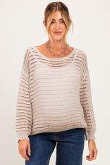 woman wearing a light beige open knit maternity sweater with a visible baby bump and casual jeans