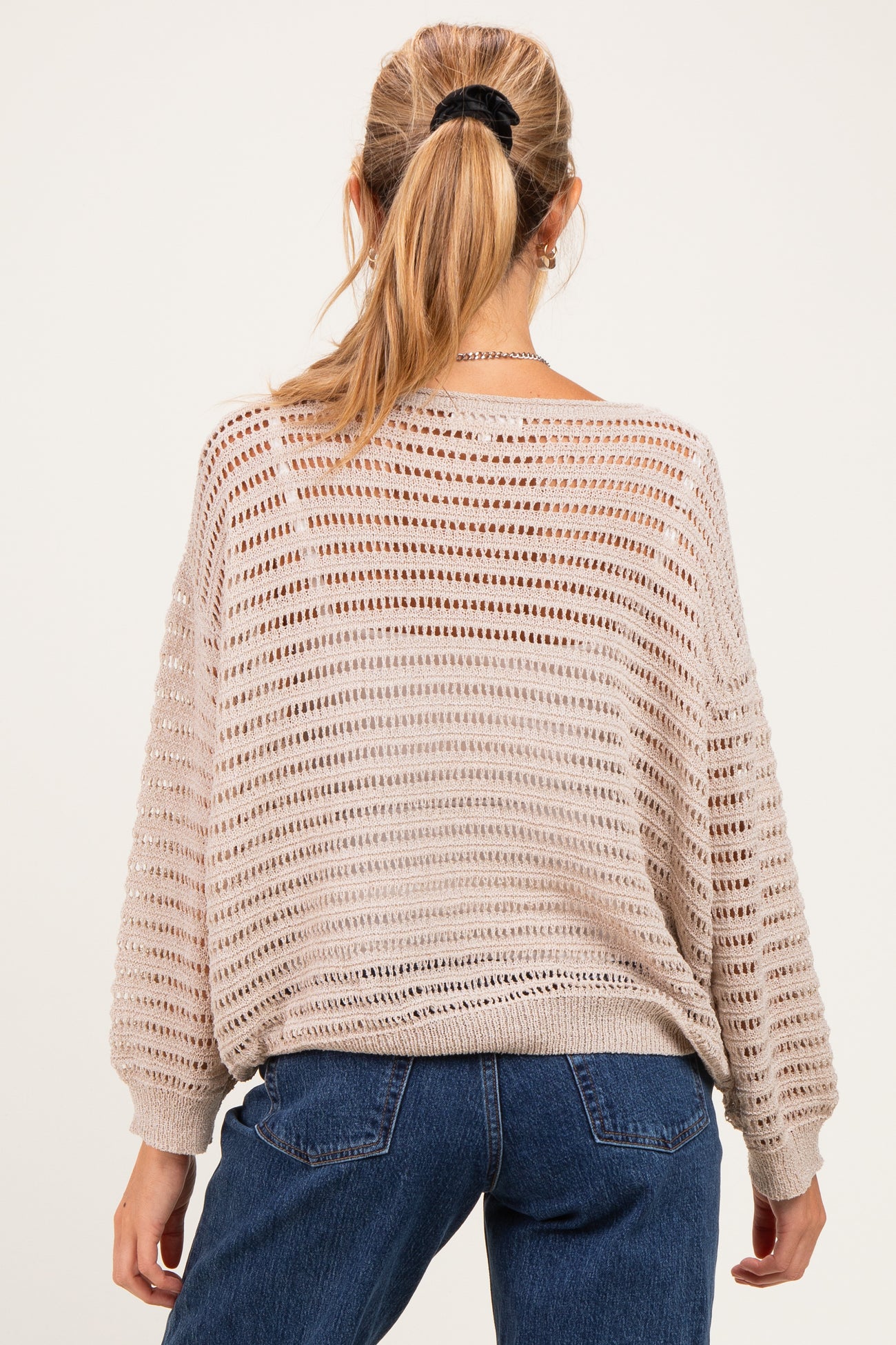 woman wearing a beige oversized knitted maternity sweater with open weave detail and back view visible