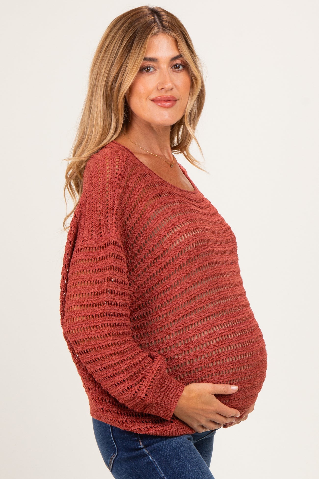 woman wearing a rust-colored crochet maternity sweater and showing her baby bump