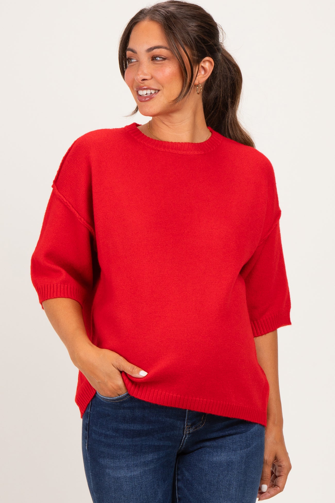 woman wearing a red oversized maternity sweater with short sleeves and a relaxed fit, smiling and touching her belly