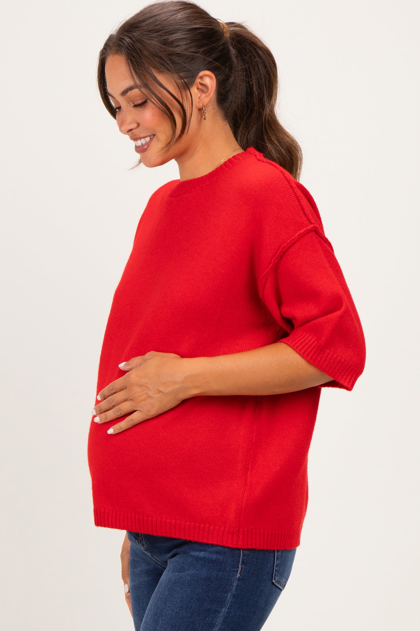 woman wearing a red short sleeve maternity sweater and holding her baby bump
