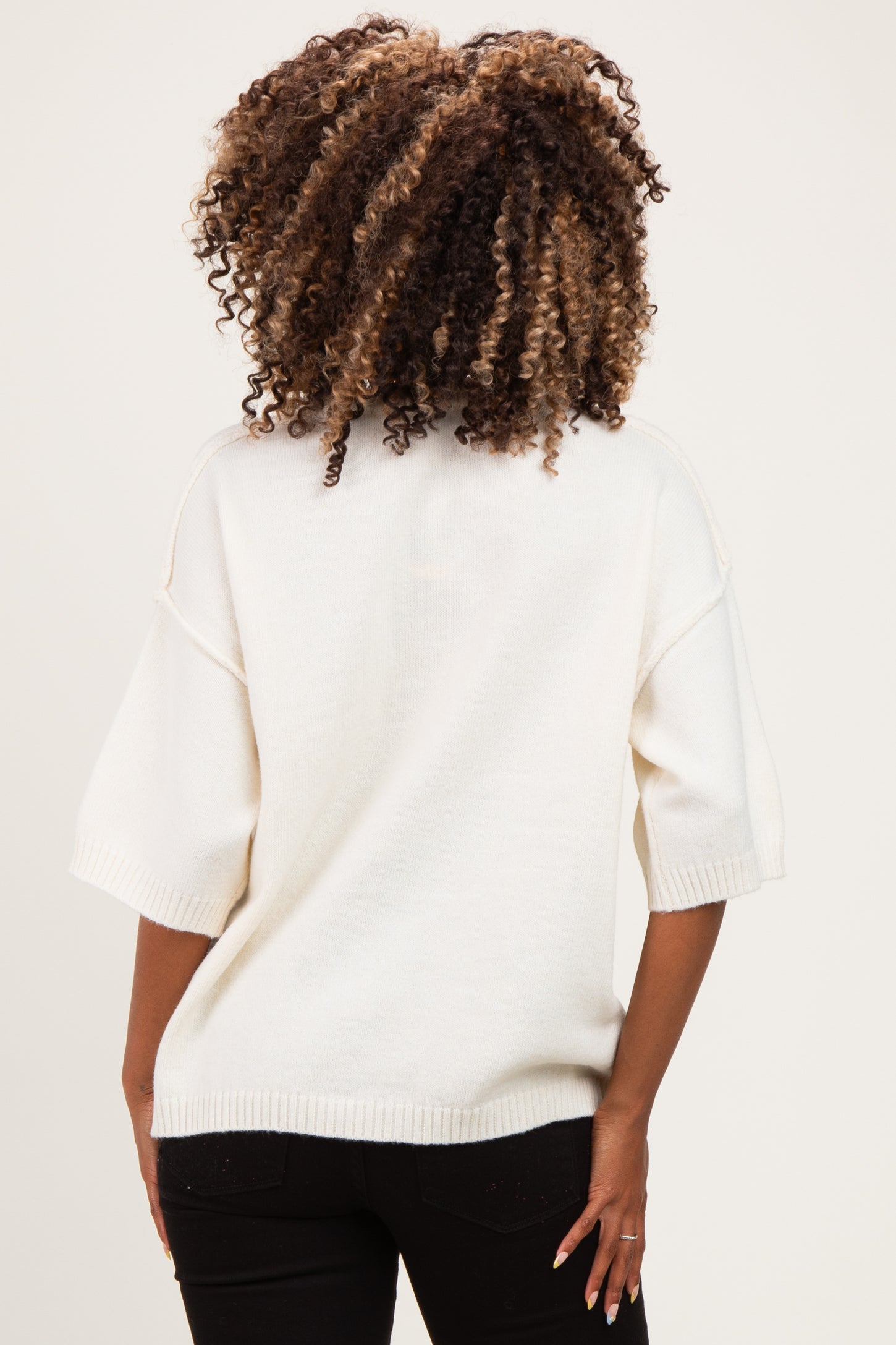 woman wearing a white oversized maternity sweater, visible from the back with curly hair and relaxed fit design