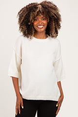 woman wearing a cream oversized maternity sweater with short sleeves and a relaxed fit, smiling and showing her baby bump