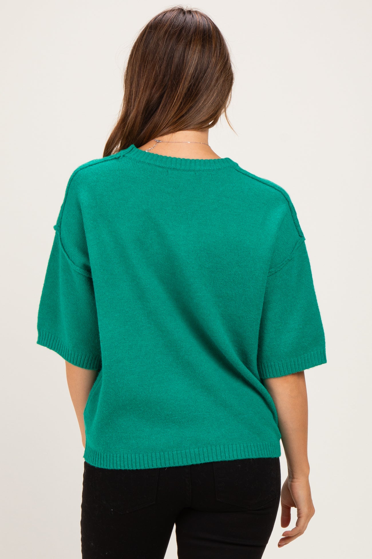 woman wearing a green short sleeve maternity sweater seen from the back