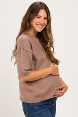 woman wearing a taupe short sleeve maternity sweater and gently cradling her baby bump