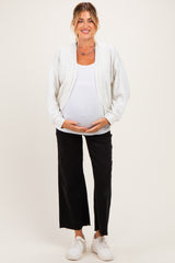 woman wearing a light gray maternity zip-up jacket over a white tank top and black wide-leg pants, showing her baby bump