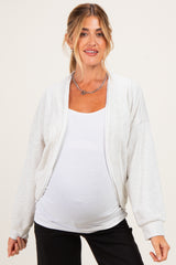 woman wearing a light grey maternity cardigan over a white tank top and showing her baby bump