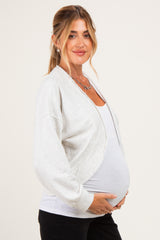 woman wearing a light gray maternity cardigan over a white top and holding her baby bump