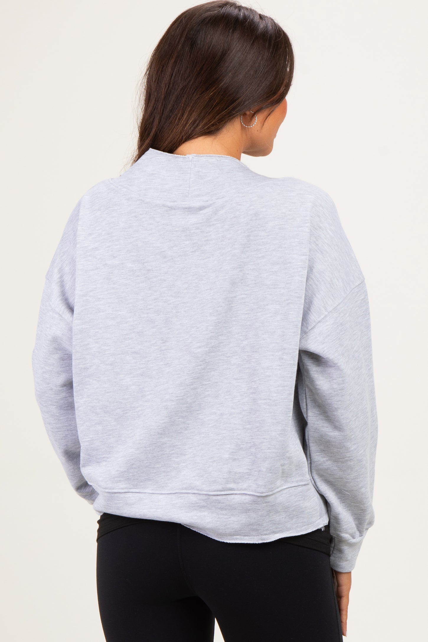 woman wearing a light grey maternity sweatshirt from the back, styled with black leggings
