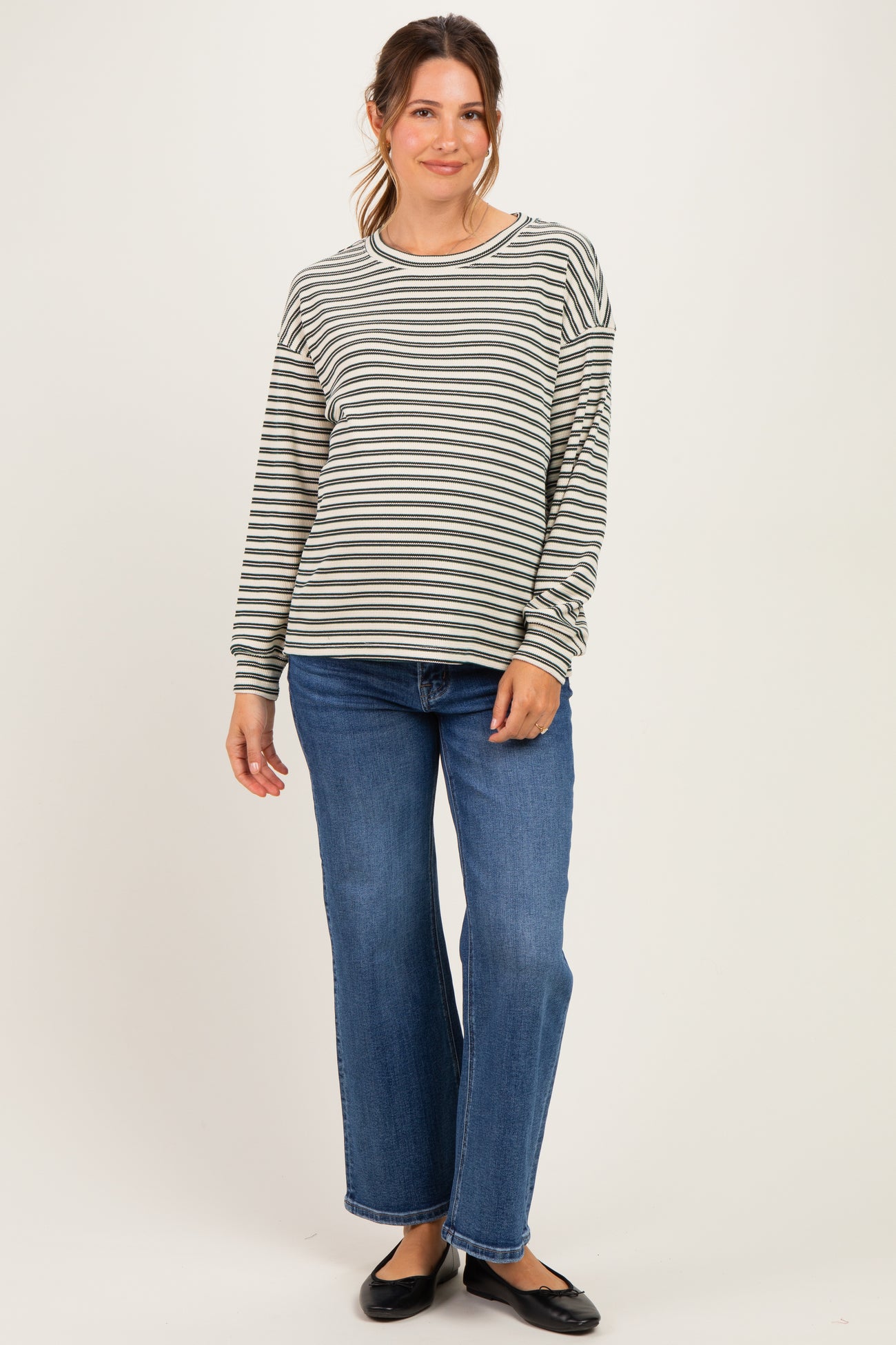 woman wearing a gray and white striped maternity top with long sleeves and blue wide-leg jeans, showing her baby bump