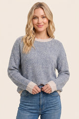 woman wearing a grey striped knit sweater with beige cuffs and holding her hands at her waist