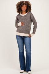 woman wearing a striped maternity sweater with a light cream hem and blue flared jeans, holding her baby bump